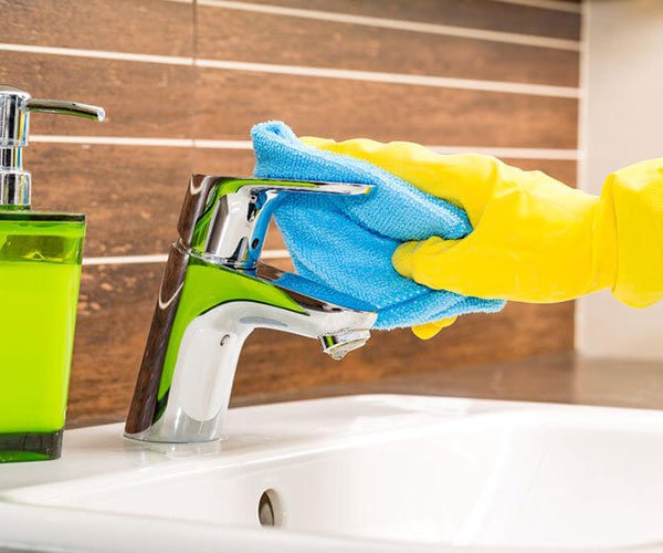Gloved hands wiping down a bathroom tap with a microfibre cloth during an end of tenancy clean