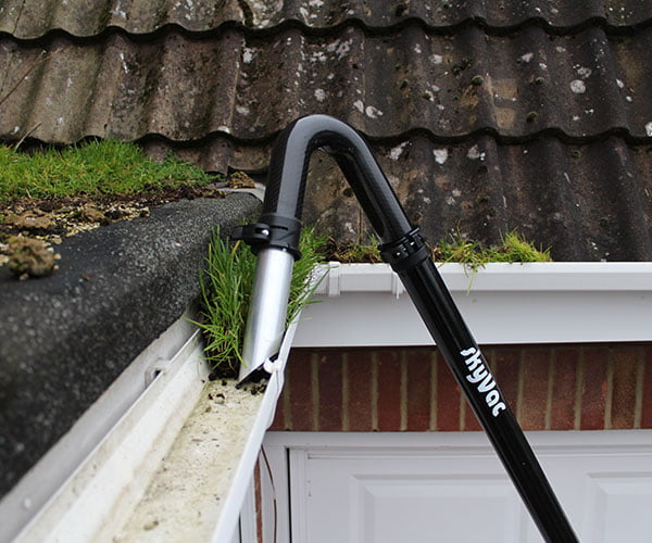 A gutter vacuum pole clearing moss and debris from a blocked gutter from ground level